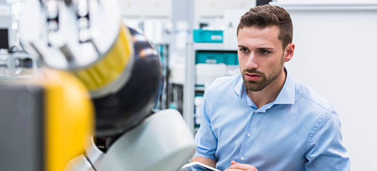 Ein Mann in einem hellblauen Hemd beobachtet konzentriert einen Roboter in einer modernen Laborumgebung.