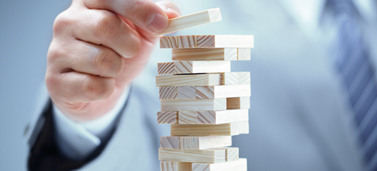 A hand placing a wooden block on top of a stack of Jenga-like blocks, with a blurred background.