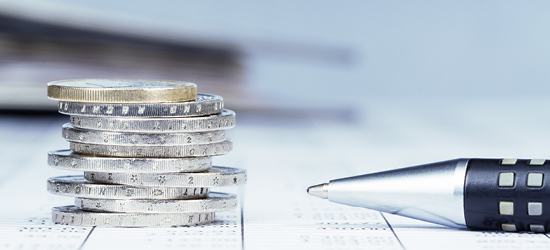 Pilas de monedas apiladas junto a un bolígrafo sobre un fondo de papel.