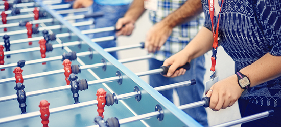 Des joueurs interagissent avec une table de baby-foot, faisant tourner les barres pour déplacer les figurines.